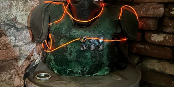 Manekin ubrany w stylu cyberpunk tj. zieloną kamizelkę, srebrne okulary oraz opleciony neonowymi kablami